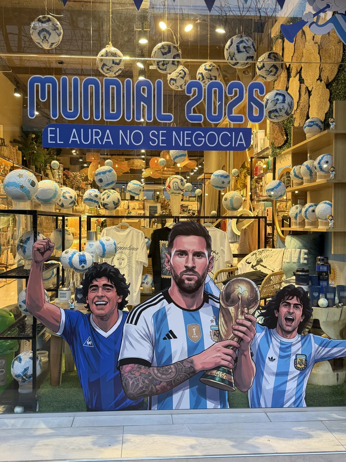 Vidriera del Mundial 2026 de Aura Home Deco: Maradona, Messi con la copa y Kempes ilustrados sobre el vidrio, con la frase El aura no se negocia