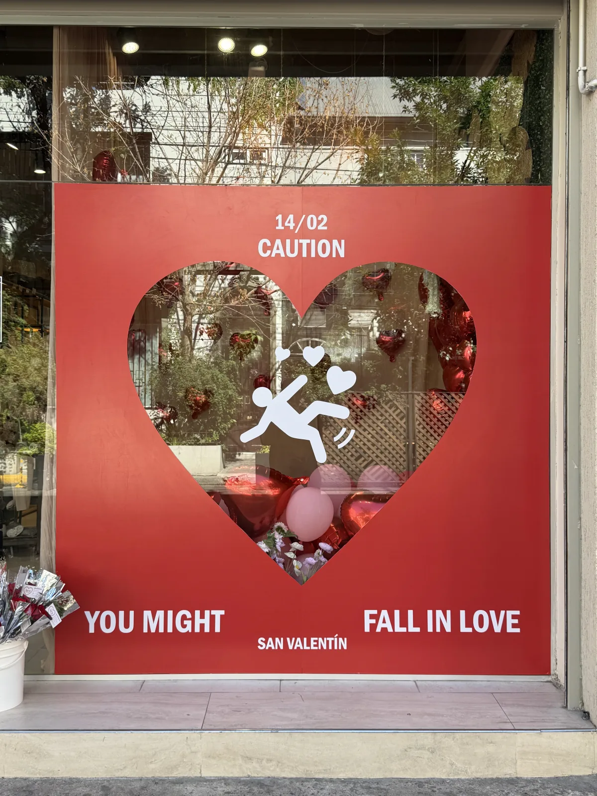 Vidriera de San Valentín de frente y de día: panel rojo con el corazón calado y la gráfica Caution, you might fall in love
