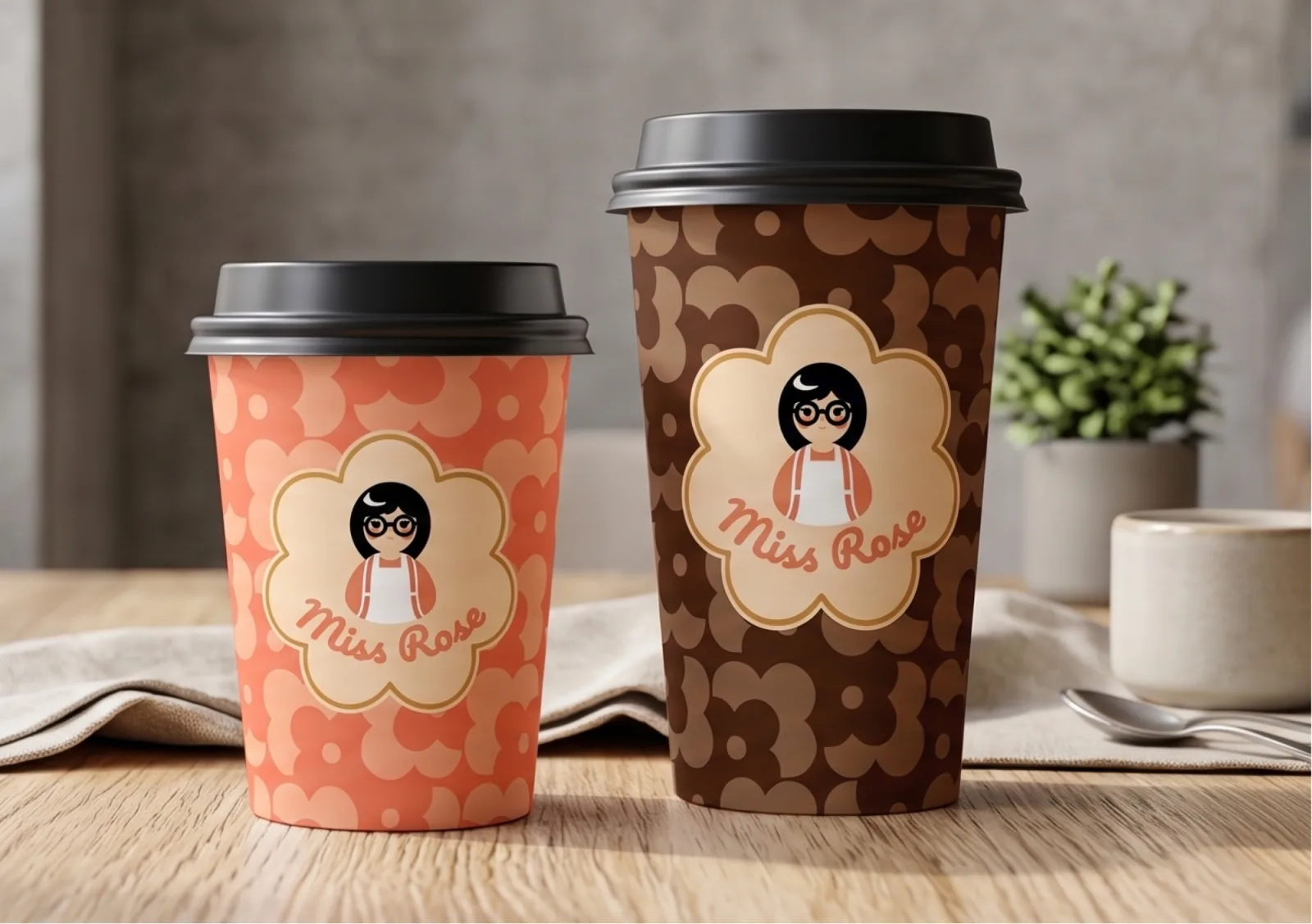Vasos de café para llevar de Miss Rose: uno coral con patrón floral y otro marrón, ambos con el sello de la marca
